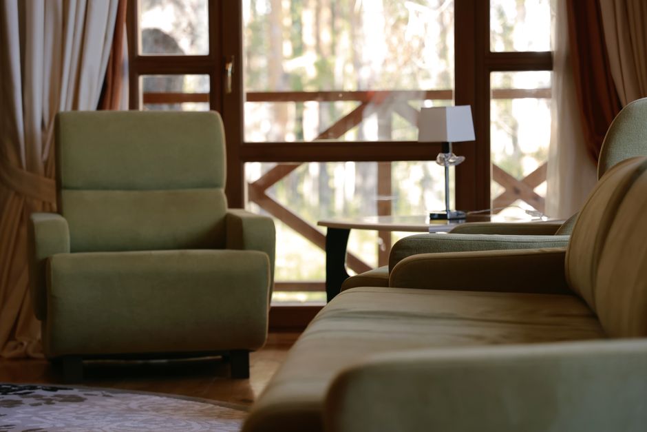 A living room corner featuring a blue upholstered sofa with a light-colored throw blanket draped over the armrest, situated against a gray wall with a decorative green plant nearby. To the right, a sm